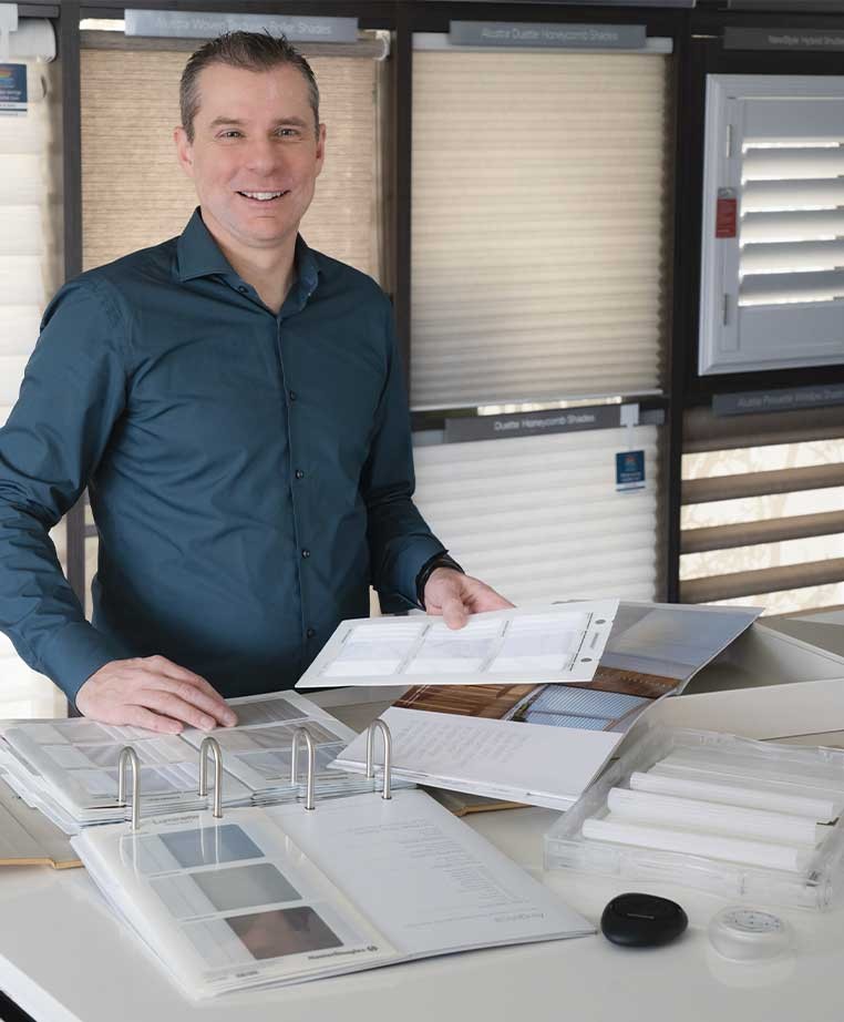 Man wearing a blue collared shirt, standing at a table covered with documents